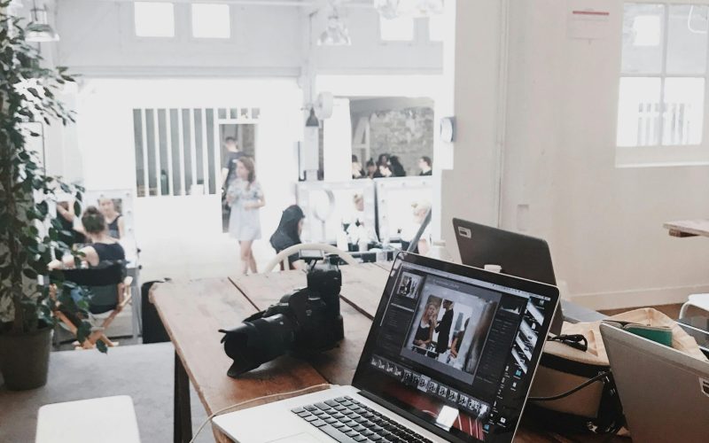 A bright, modern workspace featuring laptops, a camera, and a drawing tablet in an indoor office.